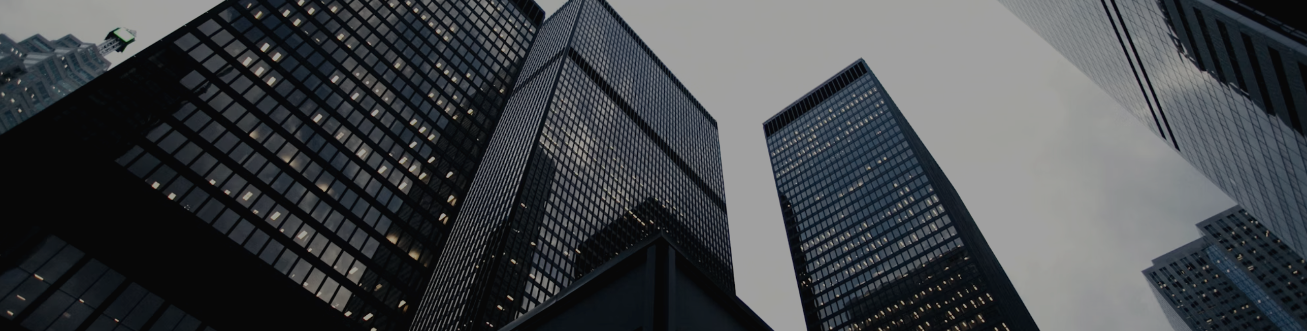 Low-angle view of dark glass office towers rising into a grey sky